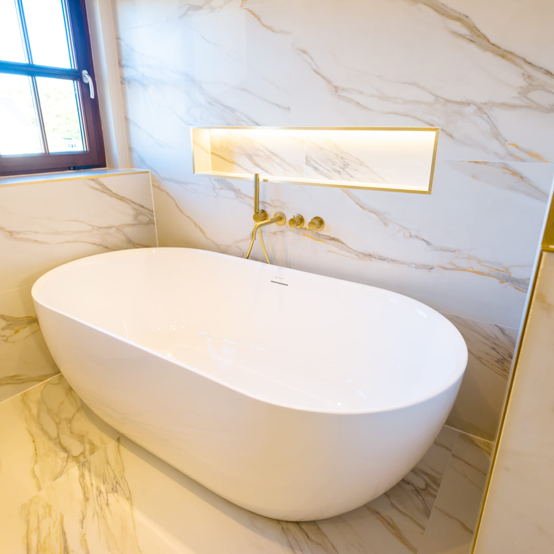 Freestanding white bath against Calacatta marble with wall-mounted brass tap