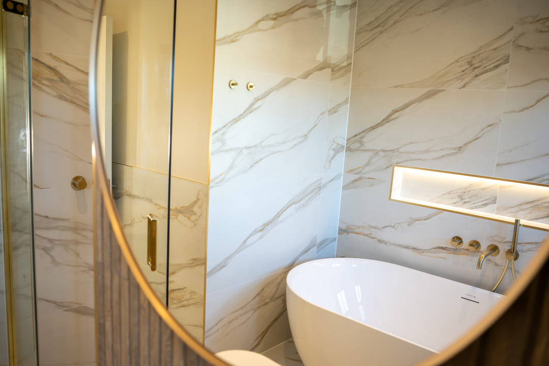 Round mirror reflecting a marble shower room and freestanding bath