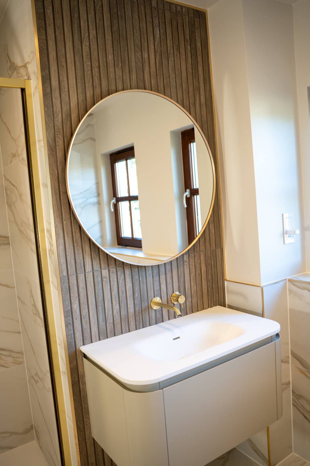 Brass wall-mounted tap over a floating basin with round mirror